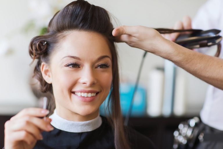 Happy woman with stylist making hairdo at salon