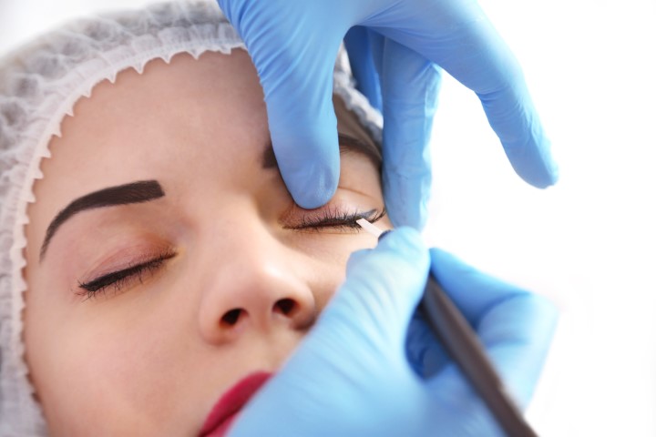 Cosmetologist applying permanent make up on eyes, close up