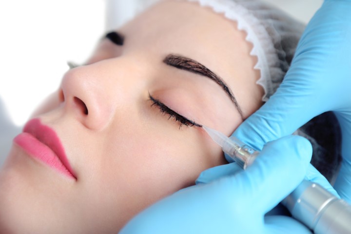 Cosmetologist applying permanent make up on eyes, close up
